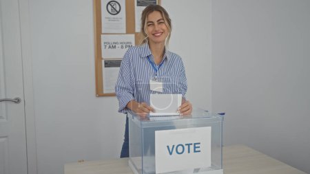 Foto de Mujer rubia sonriendo mientras inserta una boleta en una urna electoral en un centro electoral. - Imagen libre de derechos