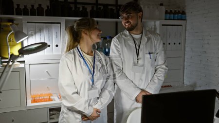Ein Mann und eine Frau, beide Wissenschaftler, lächeln und unterhalten sich in einem gut ausgestatteten Laboratorium.