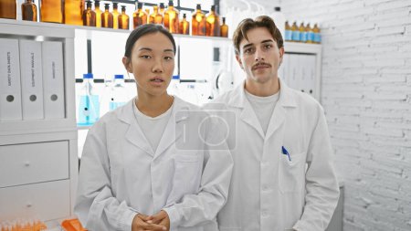 Zwei Wissenschaftler, ein Mann und eine Frau, stehen zusammen in einem mit Geräten und Bernsteinflaschen gefüllten Labor.