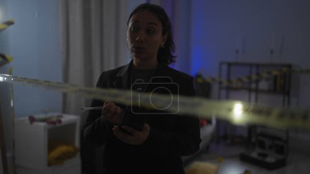 Foto de Mujer hispana detective tomando notas en una escena del crimen en el interior con cinta de precaución - Imagen libre de derechos