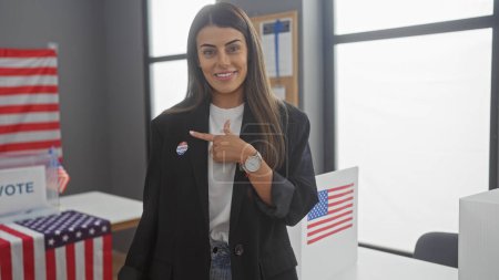 Una joven hispana con una etiqueta de 'yo voté' se apunta a sí misma en una sala de colegio electoral americana con banderas.
