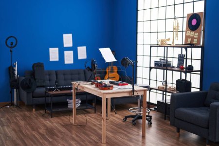Photo for A stylish music studio setup with a blue wall, featuring a guitar, microphone, headphones, and sheet music on a wooden table. - Royalty Free Image