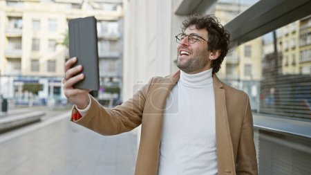 Un homme barbu joyeux prenant un selfie dans une rue animée de la ville, émettant dynamisme et mode de vie urbain.