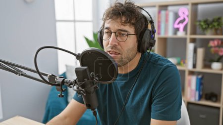 Ein junger hispanischer Mann mit Bart spricht in einem Radiostudio in ein Mikrofon und trägt Kopfhörer.