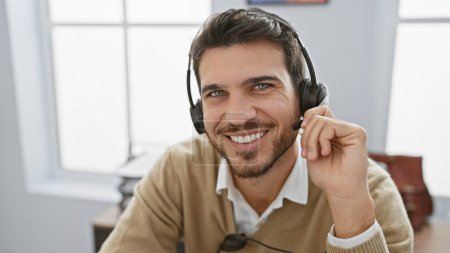 Handsome hispanic man with beard smiling in office wearing headset