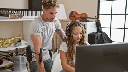 A man and woman collaborating in a music studio setting, with instruments and recording equipment.