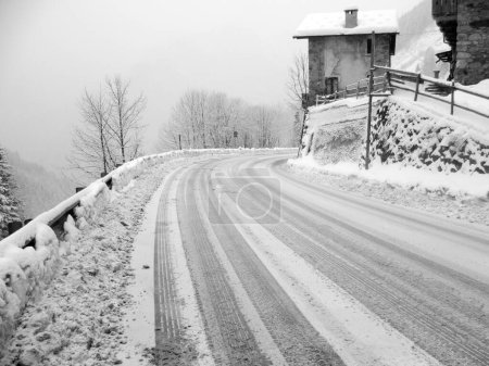 Foto de Carretera de montaña nevada con curva peligrosa y huellas de neumáticos en nieve fresca - Imagen libre de derechos