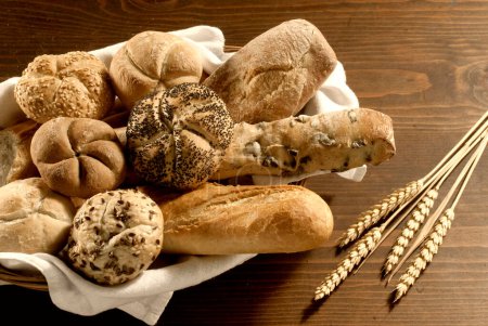Foto de Cesta con diferentes tipos de pan en una tabla de madera, con espigas de trigo - Imagen libre de derechos