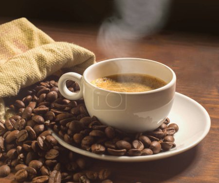 Foto de Taza de café con platillo y granos de café en toda la mesa de madera - Imagen libre de derechos