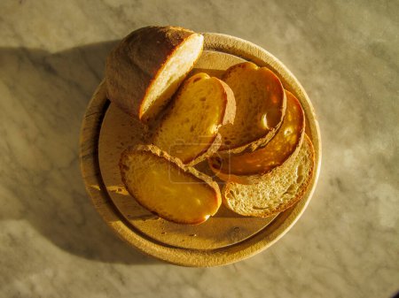 Foto de Tabla de cortar de madera redonda con rebanadas de pan a la luz del sol - Imagen libre de derechos