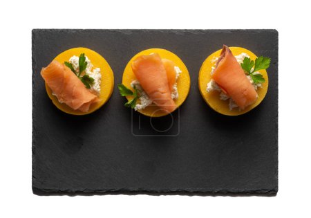 Foto de Bandeja de pizarra negra con tres porciones de polenta con salmón y queso - Imagen libre de derechos