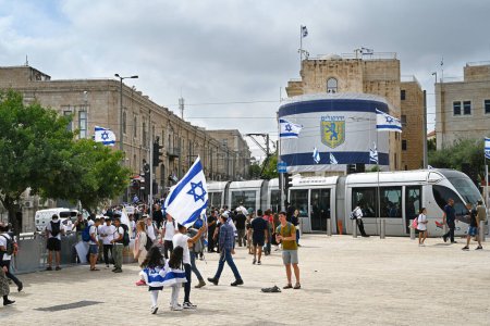 Photo for JERUSALEM, ISRAEL - MAY 18, 2023: a Light Rail passes Revelers on the IDF square in front of the Jerusalem Old Town Hall - Royalty Free Image