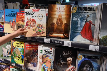Foto de WALLONIA, BÉLGICA - AGOSTO 2023: Estantes Libros de historietas en venta en la sección de lectura en un hipermercado de Carrefour en Bélgica - Imagen libre de derechos