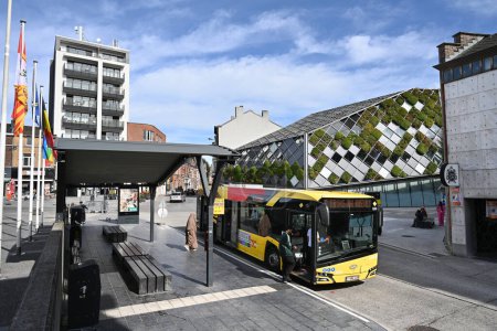 Téléchargez les photos : HERSTAL, WALLONIE, BELGIQUE - SEPTEMBRE 2023 : Les passagers montent à bord d'un bus à la gare routière. En arrière-plan l'architecture moderne de la mairie - en image libre de droit