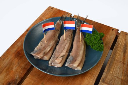 Ein Teller Heringe mit holländischen Flaggen, eine traditionelle holländische Delikatesse, auf einem Holztisch