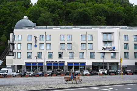 Téléchargez les photos : SPA, WALLONIA, BELGIQUE - AOÛT 2023 : L'homme est assis sur un banc sur une place devant un luxueux hôtel moderne dans les Ardennes belges - en image libre de droit