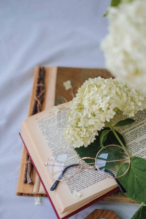 Libro abierto con flores de hortensias y gafas en la cama blanca