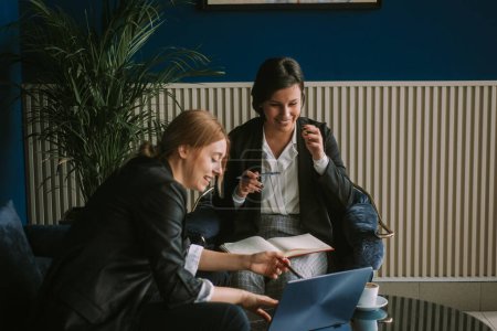 Deux busines femmes souriant et regardant l'ordinateur portable tout en étant assis au café