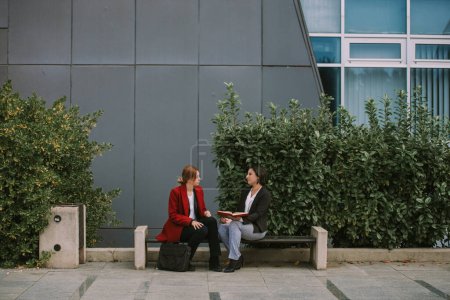 Deux belles femmes d'affaires assises sur le banc près du bâtiment