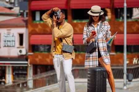 An attractive female tourist is scrolling on her phone while her boyfriend is taking a picture