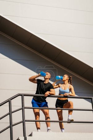 Fit couple resting after hard training. They are drinking water