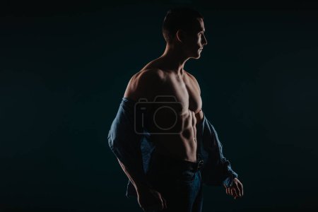 Well-built and attractive man standing in a dark room and flexing his upper body