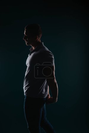 Appealing and well-built man standing in a dark room and posing