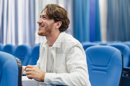 Young handsome male student joyful and cheerful smiling and being happy while sitting in the conference room