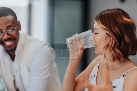 Schöne Mitarbeiterin trinkt während eines Meetings Wasser, während ihr schwarzer männlicher Kollege ihr etwas erklärt.