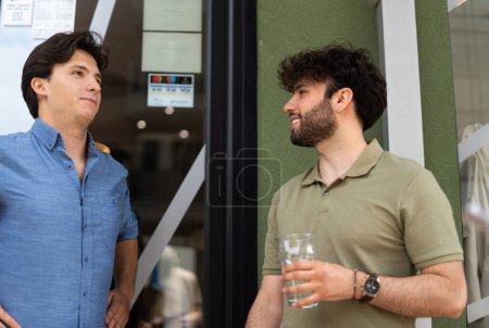 Asking a friend to confess. Hard to confess. Male employee holding a glass of water asking his coworker to confess that he likes his female colleague