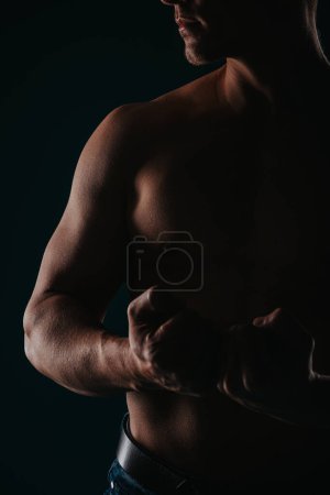 Ajuste hombre deportista posando sobre un fondo oscuro, mostrando sus bíceps, pecho y mirando a un lado