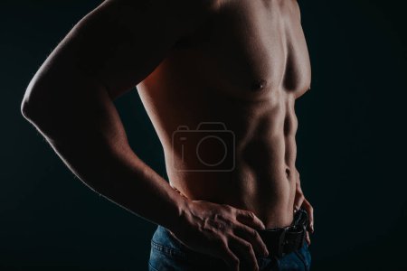 Junger muskulöser Mann mit nacktem Oberkörper posiert mit den Armen auf der Taille im Studio
