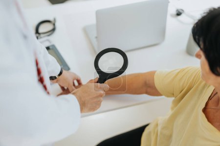 Partial, above view photo of doctor checking patient skin using magnifying glass.
