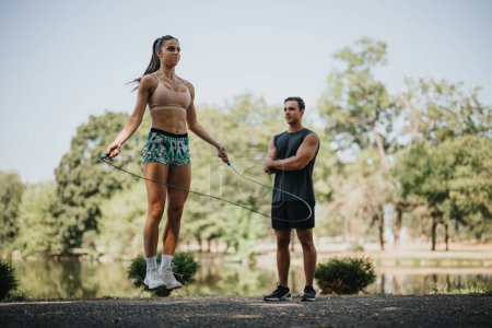 Fit friends challenge themselves with an outdoor workout in the park. They stretch and warm up before jumping rope together, motivated and persistent. Positive results await.