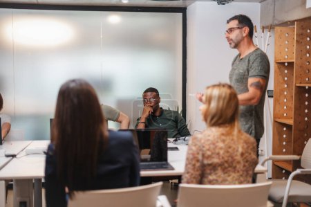 Empresario explicando nuevo proyecto a sus empleados multirraciales durante la reunión en la oficina moderna