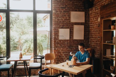 Ein kaukasischer Student genießt die freie Zeit allein in einer Kaffeebar, surft und sendet Nachrichten auf einem Smartphone und schafft eine positive und entspannte Atmosphäre.