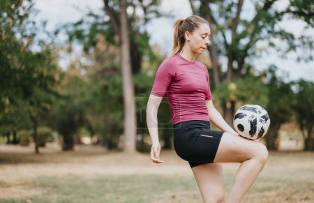 Fit woman performing juggling football freestyle tricks outdoors with a soccer ball. Enjoying sunny day in nature park.
