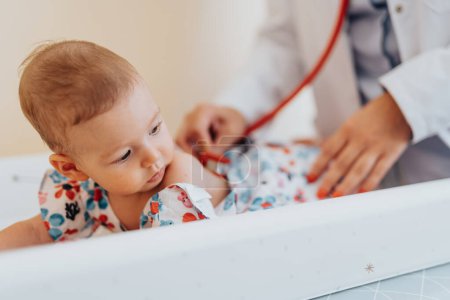 Doctor examining baby using stethoscope, providing necessary healthcare. A cute baby receives attentive healthcare from a specialist in a calm clinic.