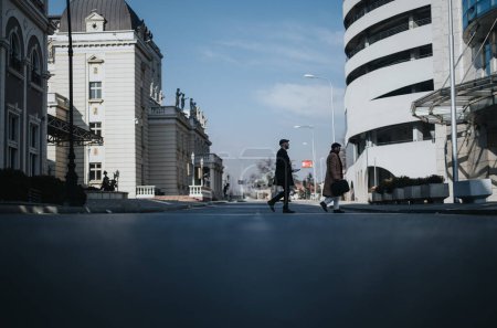 A moment captured of two individuals strolling side by side on an urban street, contrasting historical and contemporary architectural backdrops.