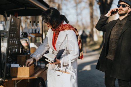 Businessman on a phone call and businesswoman with a digital tablet at an outdoor coffee cart on a clear winter day.
