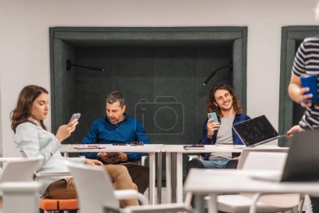 Grupo intergeneracional y diverso de empleados en un espacio de oficina moderno, interactuando con dispositivos digitales y colaborando con un sentido de camaradería.