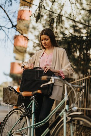 Young businesswoman opening her laptop bag beside a vintage bicycle, urban lifestyle concept