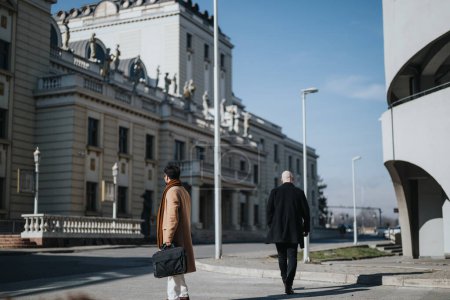 Deux hommes d'affaires en tenue formelle marchant dehors par une journée ensoleillée, juxtaposant architecture classique et design moderne.