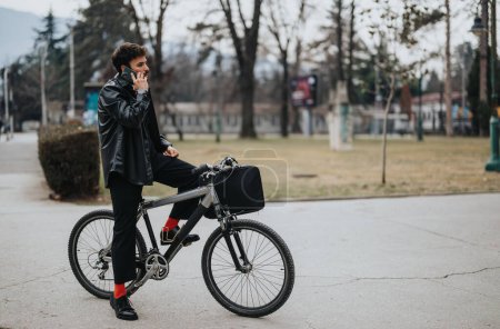 Ein junger männlicher Unternehmer führt ein Telefongespräch und macht eine Pause mit seinem Fahrrad in einem Stadtpark..