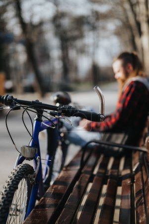 Hombre de negocios enfocado con una bicicleta trabaja remotamente en un portátil, sentado en un banco de la ciudad, encarnando la movilidad urbana y la flexibilidad.