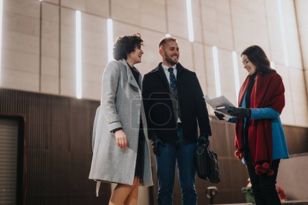 Young business professionals in warm, stylish winter clothing happily engage in conversation while walking in a modern indoor setting.