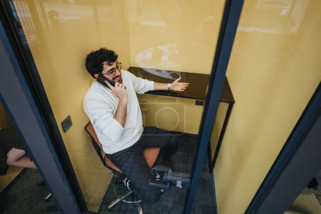 Un empleado sentado en la cabina telefónica que tiene una llamada telefónica, explicando y gestos con la mano.