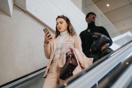 Focused young businesswoman on phone and businessman with bag riding an escalator. Modern professionals in an urban environment.