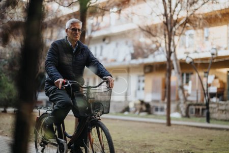 Reifer Mann mit Brille und lässiger Kleidung, der ein Fahrrad mit Korb durch einen ruhigen Stadtpark fährt und einen aktiven Lebensstil pflegt.