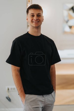 Porträt eines fröhlichen jungen erwachsenen Mannes mit kurzen Haaren, der selbstbewusst in entspannter Pose in einem lässigen schwarzen Hemd lächelt.